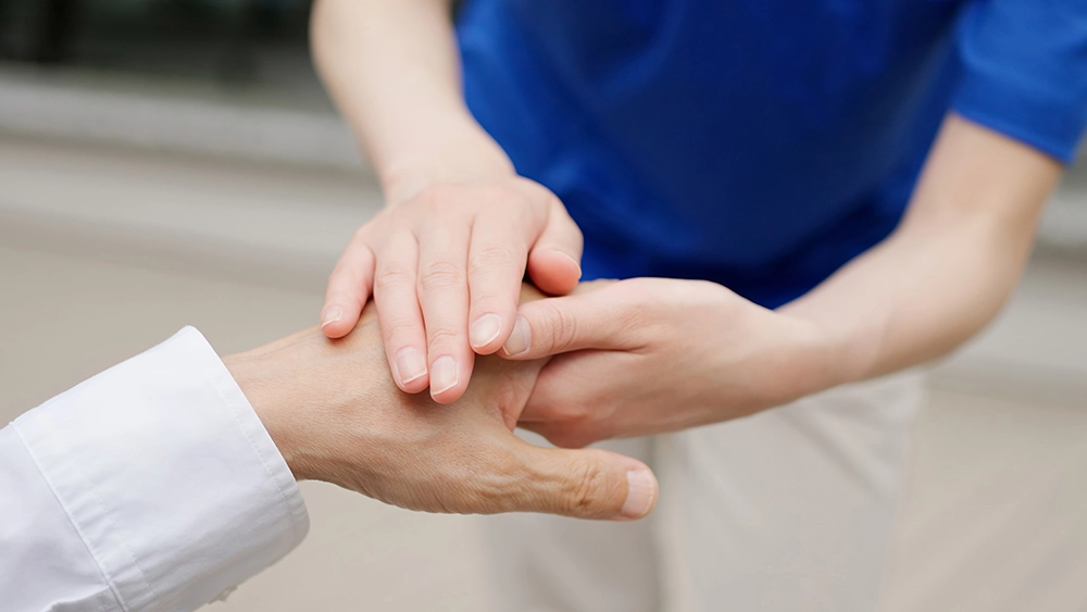 高齢者の手を優しく支えるスタッフ