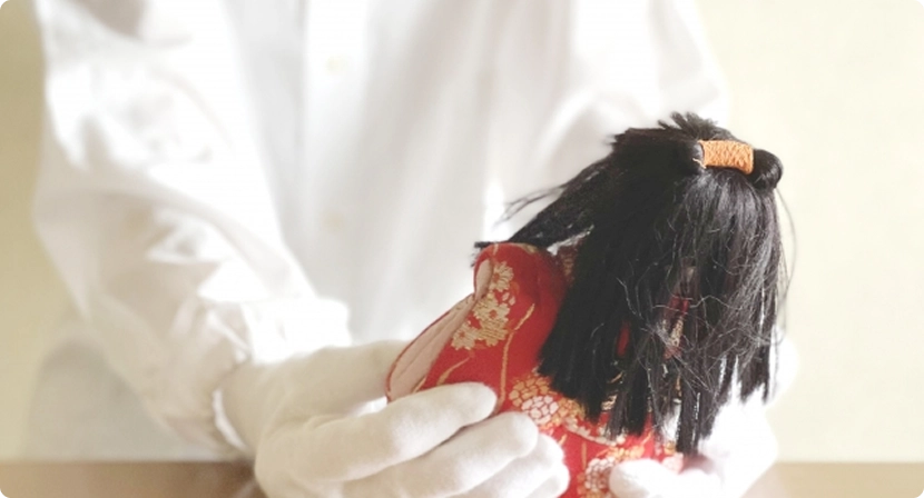 白手袋で人形を丁寧に扱うスタッフの手元